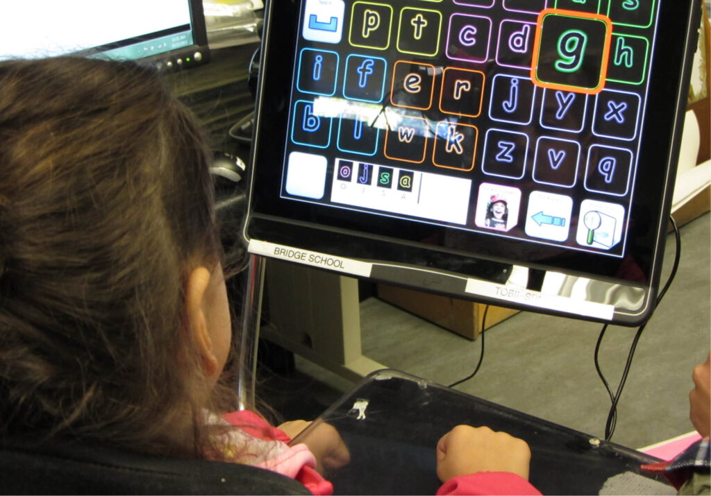 Image of a child looking at an AAC device with several letters displayed on it and the letter g is highlighted